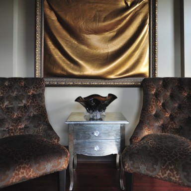 Two custom designed tufted, velvet chairs were created in leopard print paisley by PCD. They flank a handcrafted metal chest. Local Artisan, Miriam Bankey, created this sculptural painting and frame after graduating from ACA. The sand-cast glass bowl was created by Mark Gibeau. 